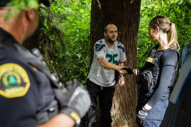 Social worker, Lauren Rainbow (right), along with Police Officer Mike Buell (left) meet a man illegally camped in the woods in Snohomish County. They are part of a new program in the county that helps people with addiction, instead of arresting them. (Leah Nash for Finding Fixes Podcast)