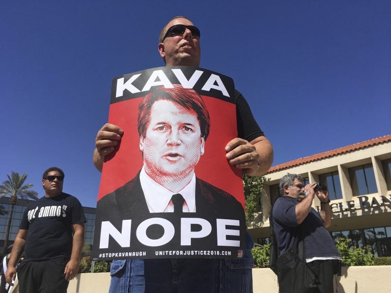 A man holds up a sign during a protest against Supreme Court nominee Brett Kavanaugh outside the offices of Arizona Sen. Jeff Flake in Phoenix, Friday, Sept. 28, 2018. (AP Photo/Patricio Espinoza)