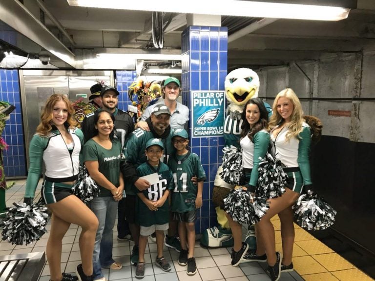 In this October 2018 photo provided by Matt Liston, Philadelphia Eagles fan Jigar Desai poses with his family, friends and members of the Philadelphia Eagles Cheerleaders in front of the subway pillar he ran into earlier this year at Ellsworth Station on the Broad Street subway line in Philadelphia. The moment in the spotlight isn’t over yet for Desai who stumbled into fame as a viral video star after running into the subway pillar. Desai is now the subject of an NFL digital short feature, shot ahead of the Oct. 28 Eagles game against the Jacksonville Jaguars in London.  (Matt Liston via AP)