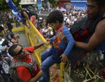 A child is carried over the border fence as thousands of Honduran migrants rush across the border towards Mexico, in Tecun Uman, Guatemala, Friday, Oct. 19, 2018. Migrants broke down the gates at the border crossing and began streaming toward a bridge into Mexico. After arriving at the tall, yellow metal fence some clambered atop it and on U.S.-donated military jeeps. Young men began violently tugging on the barrier and finally succeeded in tearing it down. (AP Photo/Oliver de Ros)