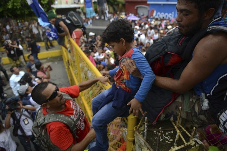 A child is carried over the border fence as thousands of Honduran migrants rush across the border towards Mexico, in Tecun Uman, Guatemala, Friday, Oct. 19, 2018. Migrants broke down the gates at the border crossing and began streaming toward a bridge into Mexico. After arriving at the tall, yellow metal fence some clambered atop it and on U.S.-donated military jeeps. Young men began violently tugging on the barrier and finally succeeded in tearing it down. (AP Photo/Oliver de Ros)