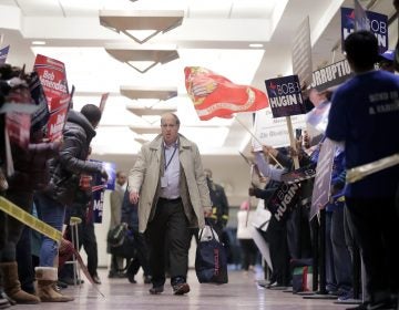 A pedestrian walks through a hallway as supporters of Democratic U.S. Senate candidate Bob Menendez, left, rallied against supporters of Republican candidate Bob Hugin outside of the NJTV Studios where the two are scheduled to engage in a debate, Wednesday, Oct. 24, 2018, in Newark, N.J. (AP Photo/Julio Cortez)