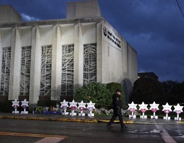In this Oct. 28, 2018, file photo a Pittsburgh Police officer walks past the Tree of Life Synagogue and a memorial of flowers and stars in Pittsburgh in remembrance of those killed and injured when a shooter opened fire during services Saturday at the synagogue. (Gene J. Puskar/AP Photo, File)