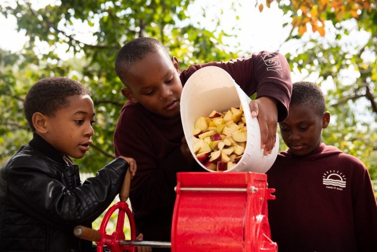 Devin Puckett, along with Clyde and Saheir Beatty, empty a bucket of apples into a fruit grinder during the East Park Apple Festival at Woodford Mansion in Fairmount Park. (Kriston Jae Bethel for WHYY)