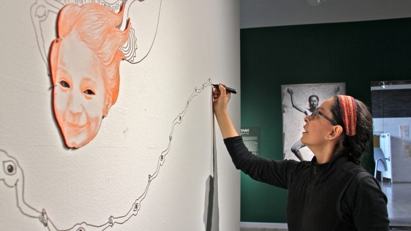 Kukulio Velarde works on a mural that will be completed during the five months that her work is on exhibit at Taller Puertorriqueno. When the exhibit ends, she will repaint the wall white. (Emma Lee/WHYY)