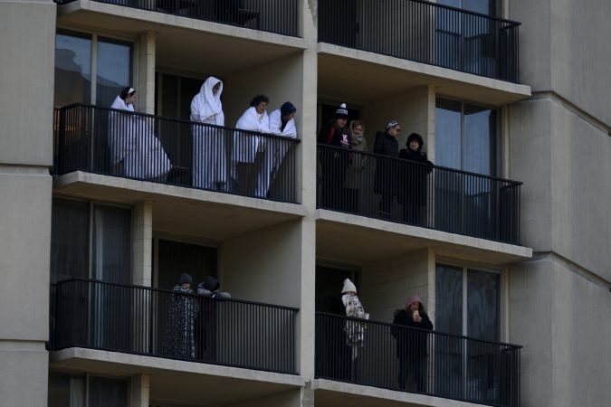 People wrapped in blankets watch from balconies as low temperatures caused a smaller than usual turnout during the 99th annual Thanksgiving Day Parade, in Center City Philadelphia. (Bastiaan Slabbers for WHYY)