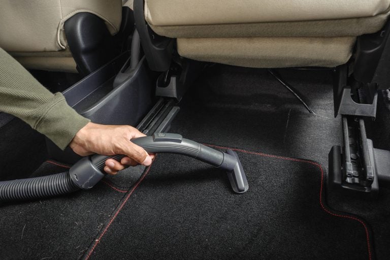 A man cleans the carpet in his car with vacuum cleaner. (Bigstock Image)