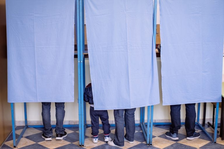 Color image of unidentifiable persons voting in booths at a polling station, during elections.