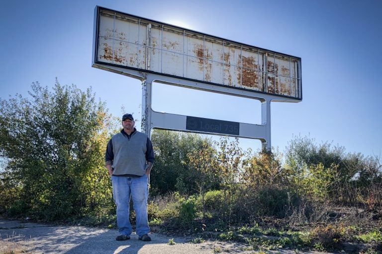 Don Skidmore stands in front of a sign for United Auto Workers Local 735, the union chapter he represented as president when he was a General Motors employee. (Ari Shapiro/NPR)
