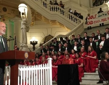 Wolf makes a speech in front of the Capitol Christmas tree as protesters display a banner telling him not to be a grinch. (Katie Meyer/WITF)