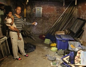 Sherri Lee, holding her 2-year-old daughter, Aubrey Boyd, shines a light on possessions that were destroyed when a backed up toilet flooded her basement. (Emma Lee/WHYY)