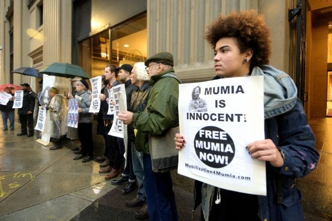 A group of two dozen activists briefly blocks traffic during a rally outside the Philadelphia district attorney’s office on Friday. The group is urging District Attorney Larry Krasner to let stand  a Common Pleas Court ruling that allows Mumia Abu-Jamal to file an appeal. (Bastiaan Slabbers for WHYY)