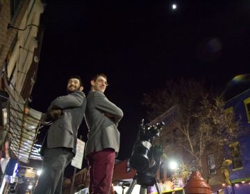 Bill Green (left) and Brendan Happe are amateur astronomers who invite people on the streets of Philadelphia to gaze at the moon through a telescope. (Kimberly Paynter/WHYY)