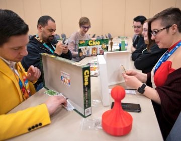 A group of convention goers, some dressed as Colonel Mustard, Miss Scarlett and Mrs. Peacock, participate in a Clue tournament at PAX Unplugged.)