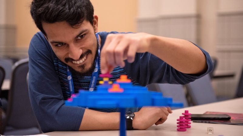 Jason Collado carefully stacks a game piece while playing Topple. (Kriston Jae Bethel for WHYY)