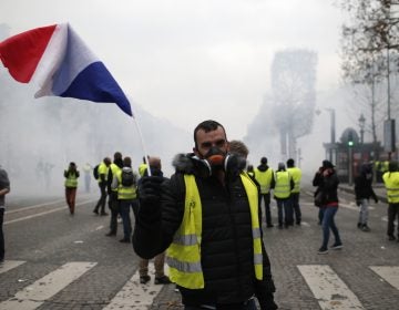 A demonstrator waves a French flag on the Champs-Elysees avenue Saturday, Dec. 8, 2018 in Paris. Crowds of yellow-vested protesters angry at President Emmanuel Macron and France's high taxes tried to converge on the presidential palace Saturday, some scuffling with police firing tear gas, amid exceptional security measures aimed at preventing a repeat of last week's rioting. (Rafael Yaghobzadeh/AP)