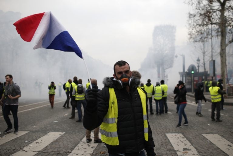 A demonstrator waves a French flag on the Champs-Elysees avenue Saturday, Dec. 8, 2018 in Paris. Crowds of yellow-vested protesters angry at President Emmanuel Macron and France's high taxes tried to converge on the presidential palace Saturday, some scuffling with police firing tear gas, amid exceptional security measures aimed at preventing a repeat of last week's rioting. (Rafael Yaghobzadeh/AP)