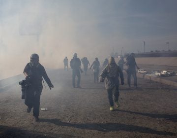 Migrants run from tear gas launched by U.S. agents, amid photojournalists covering the Mexico-U.S. border, after a group of migrants got past Mexican police at the Chaparral crossing in Tijuana, Mexico, Sunday, Nov. 25, 2018. (AP Photo/Rodrigo Abd)