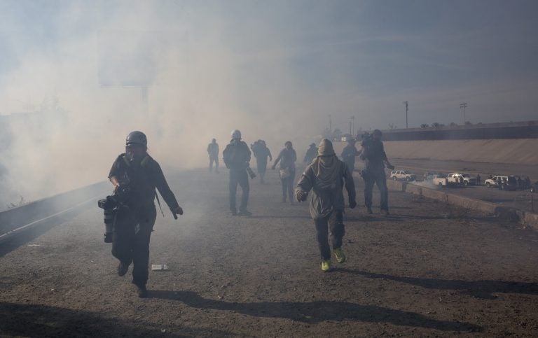 Migrants run from tear gas launched by U.S. agents, amid photojournalists covering the Mexico-U.S. border, after a group of migrants got past Mexican police at the Chaparral crossing in Tijuana, Mexico, Sunday, Nov. 25, 2018. (AP Photo/Rodrigo Abd)