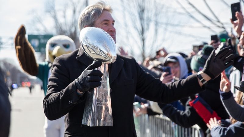 Coach Doug Pederson high-fives fans while carrying the Vince Lombardi trophy on Broad Street during the Philadelphia Eagles Super Bowl Championship parade on Feb. 8, 2018. (Lindsay Lazarski/WHYY)