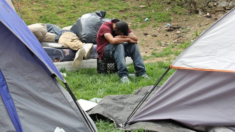 A man rests his head on his arms in a heroin encampment in a vacant lot on Kensington Avenue on May 4, 2018. The encampment was later cleared out by the city. (Emma Lee/WHYY)