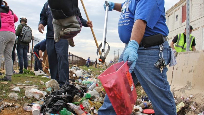 Tony Beltram of HACE separates the syringes from the rest of the trash on April 13, 2018, during the clean-up of a block-long stretch of grass between Gurney Street and the Conrail tracks, which once hosted a heroin encampment. (Emma Lee/WHYY)