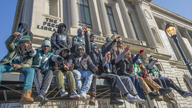 Fans cheer from atop a SEPTA bus shelter during the Super Bowl parade in Philadelphia. (Jonathan Wilson for WHYY)