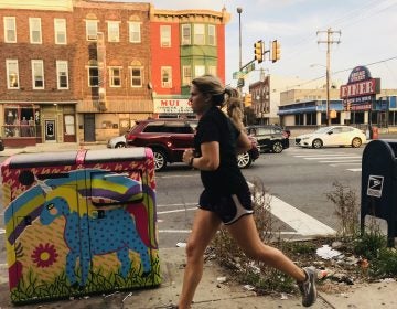 A woman runs past a pile of litter next to a Big Belly trash can on South Broad Street. (Ariella Cohen/WHYY)