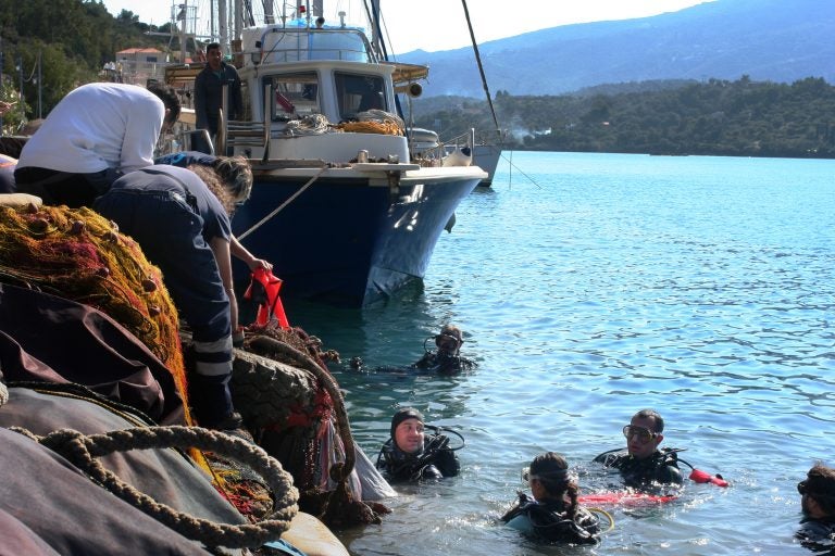 Aegean Rebreath founder George Sarelakos (center) hands a netted bag of marine litter to volunteers on the main pier of the Greek island of Poros. (Joanna Kakissis for NPR)
