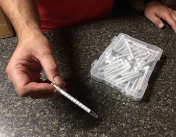 Chris holds a plastic syringe he and his wife use to administer homemade medical marijuana oil to their 13-year-old son, Dylan, who has autism.
(Lynn Arditi/The Public's Radio)