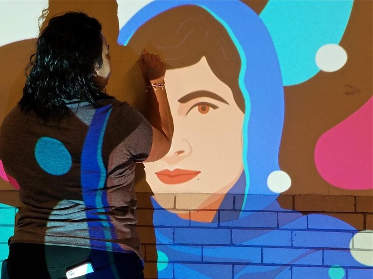 Anisa Shafiq uses a slide projector to mark out a mural of Malala Yousafzai in a hallway of Kensington High School.