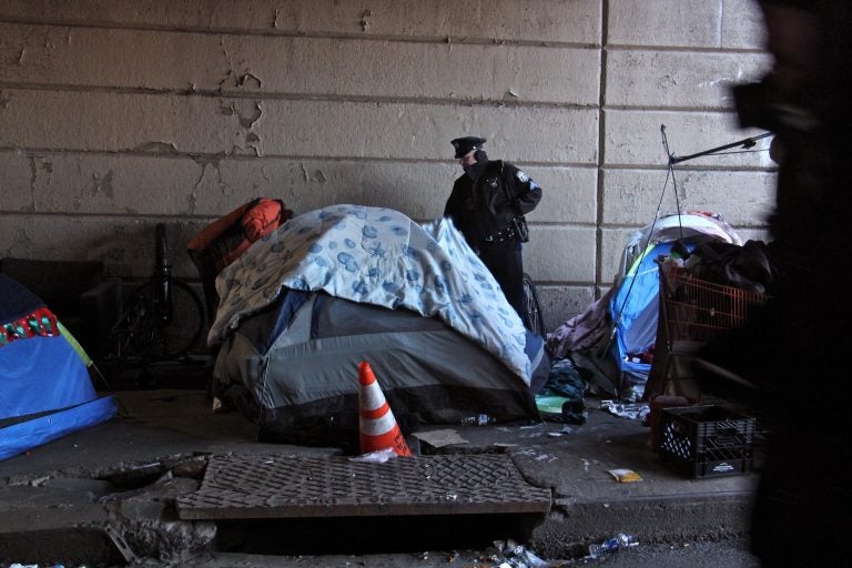 A Philadelphia police officer moves from tent to tent telling residents of the Emerald Street encampment that it's time to go. (Emma Lee/WHYY)