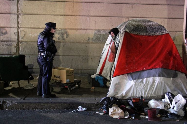 A Philadelphia police officer moves from tent to tent telling residents of the Emerald Street encampment that it's time to go. (Emma Lee/WHYY)