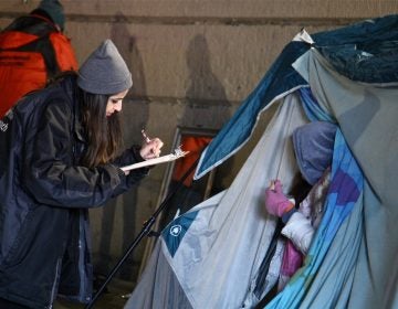 An outreach worker gets information from a woman living in a tent under the Emerald Street railroad overpass. (Emma Lee/WHYY)