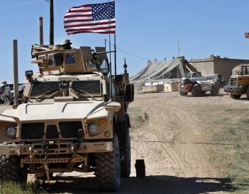 FILE - In this Wednesday, April 4, 2018 file photo, a U.S. soldier, left, sits on an armored vehicle behind a sand barrier at a newly installed position near the front line between the U.S-backed Syrian Manbij Military Council and the Turkish-backed fighters, in Manbij, north Syria. An American military official said Friday, Jan. 11, 2019 that the U.S.-led military coalition has begun the process of withdrawing troops from Syria. (AP Photo/Hussein Malla, File)