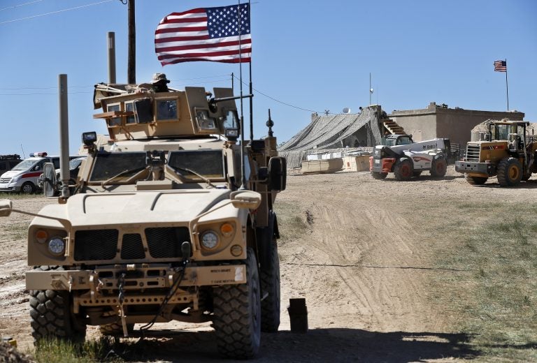 FILE - In this Wednesday, April 4, 2018 file photo, a U.S. soldier, left, sits on an armored vehicle behind a sand barrier at a newly installed position near the front line between the U.S-backed Syrian Manbij Military Council and the Turkish-backed fighters, in Manbij, north Syria. An American military official said Friday, Jan. 11, 2019 that the U.S.-led military coalition has begun the process of withdrawing troops from Syria. (AP Photo/Hussein Malla, File)
