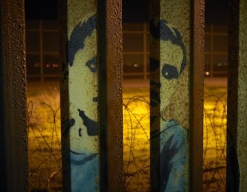 An image of a boy is painted on the bars of the border wall, in front of coils of razor wire, seen from Tijuana, Mexico. President Trump's proposal to end the partial government shutdown includes funding for more border wall, but also provisions that further restrict asylum seekers.