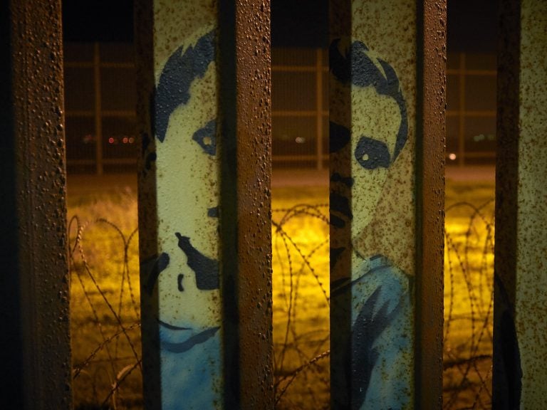 An image of a boy is painted on the bars of the border wall, in front of coils of razor wire, seen from Tijuana, Mexico. President Trump's proposal to end the partial government shutdown includes funding for more border wall, but also provisions that further restrict asylum seekers.