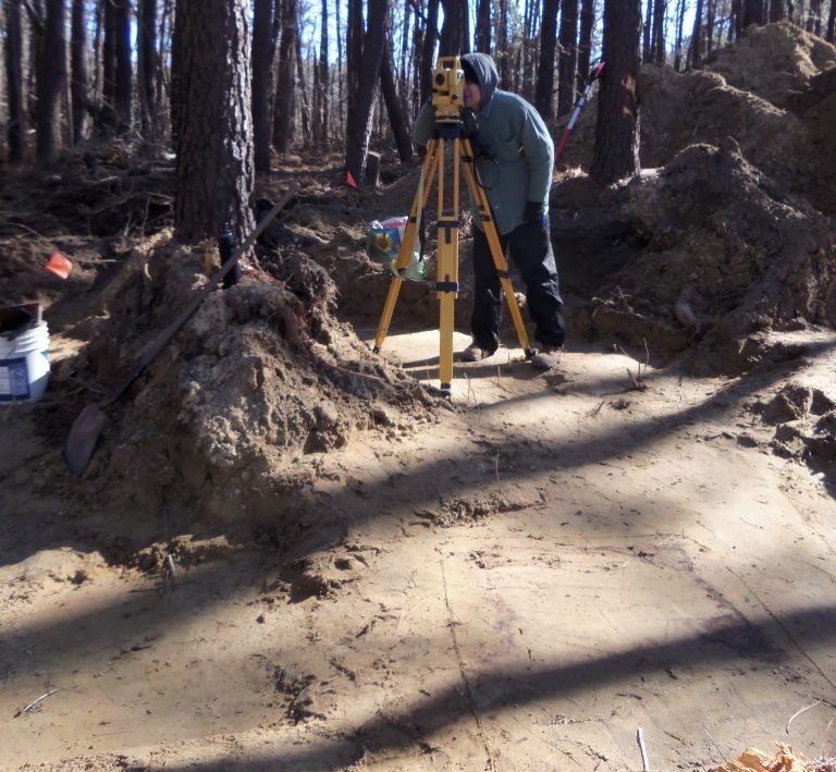 John Potts is using a total station to map the site. Graves can be seen  as grey-ish stains in the soil. (Jill Showell/Edward Otter, Inc.)