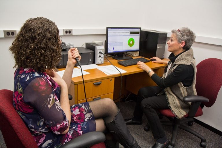 Ann Addis, Temple University clinical instructor and speech pathologist, (right) demonstrates how pitch is measured in the lab. (Kimberly Paynter/WHYY)