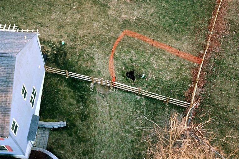 A sinkhole that opened up in January outside a suburban home at Lisa Drive in West Whiteland Township, Chester County, is surrounded by orange plastic fencing.(Eric Friedman)