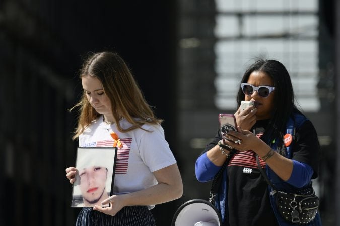 Alex Franzino, 17, March For Our Lives Philadelphia Director of Operations, holds a picture of the nephew of Roz Pichardo, while she reads out names of people killed in Philadelphia, during an anti-gun violence rally at LOVE Park on Sunday. (Bastiaan Slabbers for WHYY)