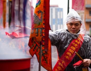Zhang Wen tosses lit firecrackers into a barrel as part of the Hoyu Folk Culture Festival parade in Philadelphia's Chinatown on Sunday, March 31, 2019. (Kriston Jae Bethel for WHYY)