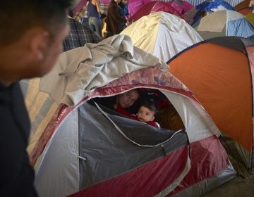 In this March 5, 2019, image, Ruth Aracely Monroy, (center), looks out of the family's tent alongside her 10-month-old son, Joshua, as her husband, Juan Carlos Perla, (left), passes inside a shelter for migrants in Tijuana, Mexico. (Gregory Bull/AP Photo)