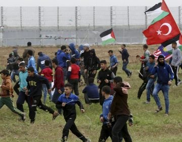 Protesters run to cover from teargas fired by Israeli troops near fence of Gaza Strip border with Israel on Saturday. The day marked the first anniversary of the Gaza border protests. (Adel Hana/AP Photo)