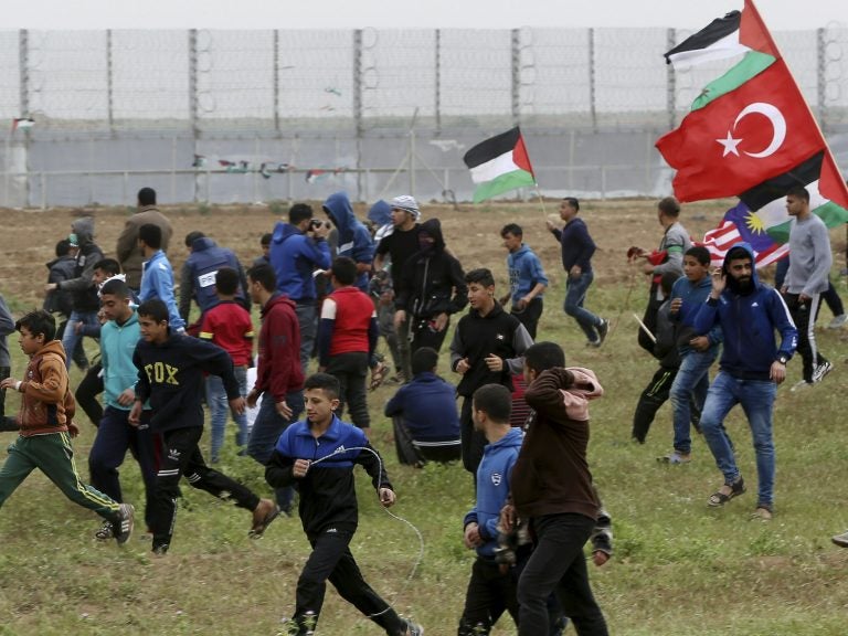 Protesters run to cover from teargas fired by Israeli troops near fence of Gaza Strip border with Israel on Saturday. The day marked the first anniversary of the Gaza border protests. Protesters run to cover from teargas fired by Israeli troops near fence of Gaza Strip border with Israel on Saturday. The day marked the first anniversary of the Gaza border protests. (Adel Hana/AP Photo)