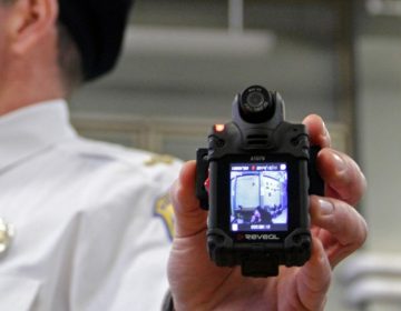 A Delaware police officer holds up a body camera.