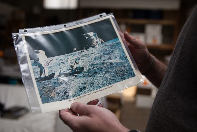 J.J. Tiziou holds a print of the moon landing signed by Buzz Aldrin, Neil Armstrong and Michael Collins.  The photograph is part of his late father, French journalist Jacques Tiziou’s, collection of memorabilia from the Apollo missions and space program. (Lindsay Lazarski/WHYY)