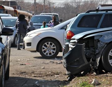 Students from Southwest Leadership Academy are seen in this 2019 file photo navigating a sidewalk near the school congested with wrecked cars and debris associated with two auto repair shops on the block. (Emma Lee/WHYY)