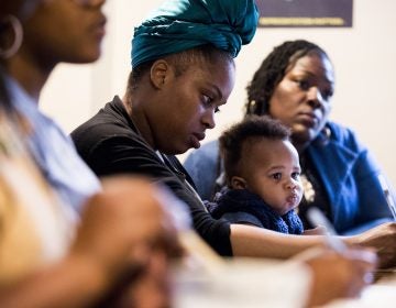 Thaashae Reingoud (center) takes notes as her son, Amir, sits on her lap at the 